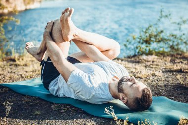 Genç sakallı adam yoga yapıyor ve Asana 'da duruyor. Güzel dağ taş ocağı gölü manzarası. Karmaşık ve komik yoga filmi. Uluslararası Yoga Günü