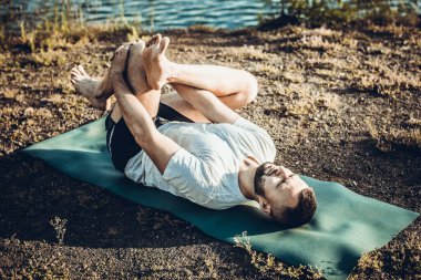 Sabah parkında yoga yapan genç bir adam. Sakallı adam rahatla ve doğada esne. Uluslararası Yoga Günü