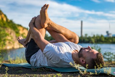 Sabah parkında yoga yapan genç bir adam. Sakallı adam rahatla ve doğada esne. Uluslararası Yoga Günü