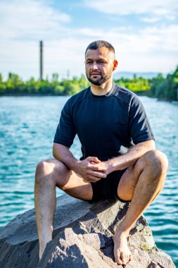 Taş ocağının arka planında kayaların üzerinde oturan sakallı genç adam. Yakışıklı portre..