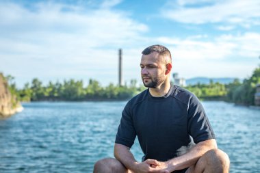 Taş ocağının arka planında kayaların üzerinde oturan sakallı genç adam. Yakışıklı portre..
