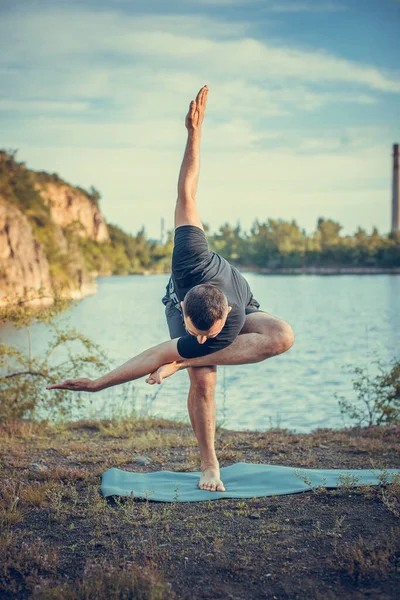 A good looking young bearded man doing yoga on quarry lake backdrop. International Day of Yoga concept.