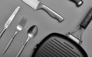 Gri bir masada siyah bıçaklar, ızgara tepsisi, havlu. Düz konum, kopyalama alanı ile yerleşim.