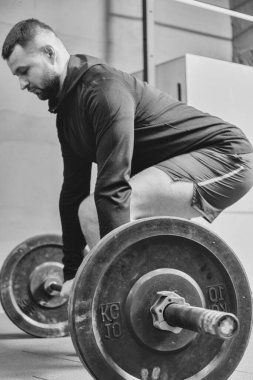 Spor kıyafetli genç bir adam spor salonunda antrenman yaparken ağırlık kaldırmaya hazırlanıyor. Fitness sporu veya sağlıklı yaşam tarzı konsepti.