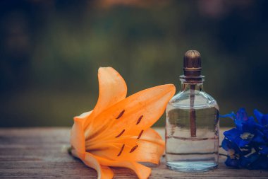 Arka planda çiçekler olan parfüm şişesi. Etiketli parfüm şişesi ve masada küçük çiçekler..