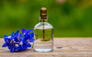 Arka planda çiçekler olan parfüm şişesi. Etiketli parfüm şişesi ve masada küçük çiçekler..