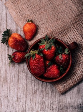 Kahverengi bir kasede taze çilekler ahşap bir masada, kırsal tarzda, seçici bir odak.