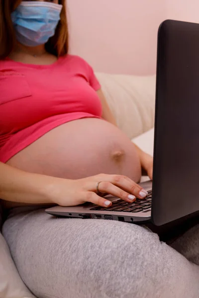 Pregnant woman with belly using a laptop on the bed. Concept of Smart working due to the quarantine for covid19 coronavirus. Stay at home office and work. High resulotion image.