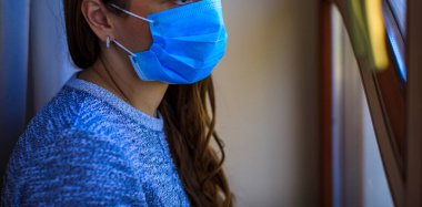 Yüzünde maskeyle pencerede duran bir kadın. Evde kal. Kendini izole etmek Covid-19 'u durdurmanın tek yolu. Evde kalıp Coronavirus 'u karantinaya alın. Yüksek resulotion resmi.