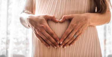 Hamile bir kadın bebeğinin karnında elini kalp şeklinde tutuyor. Parmakları kalp sembolü olan hamile bir karın. Annelik konsepti. Bebek partisi. Yüksek resulotion resmi.