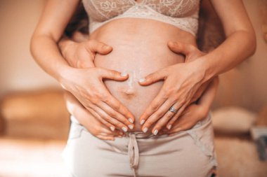 Anne ve babanın elleri hamile annenin karnında kalp yapıyor. Elleri bebeğin üzerinde olan anne ve baba. Yüksek resulotion resmi.