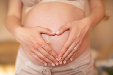 Karı ve kocanın eli, hamile karnında kalp oluşturur.