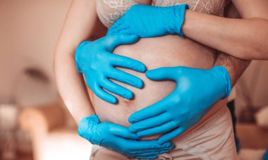 Elleri bebeğin üzerinde olan anne ve baba. Kordemik Coronavirus ya da COVID-19 'dan korunmak için mavi eldiven takan kendini izole edilmiş hamile bir kadın. Yüksek resulotion resmi.