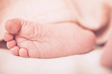 Hafif bir battaniyeye sarılı şirin bebek bacakları. Hafif bir arka planda uyuyan bebek. Yenidoğan bacakları. Bebek eşyaları paketleme şablonu. Tıbbi ve sağlıklı bir kavram. Resmi kapat.