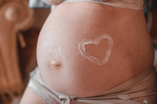 A closeup of a pregnant woman\'s tummy, with a heart drawn around her belly button.