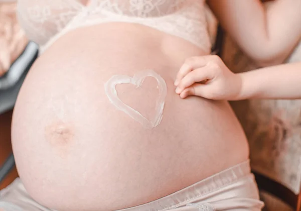 Heart shape painted with creme on belly of pregnant woman. Closeup of pregnant woman holding her belly. High resulotion image.