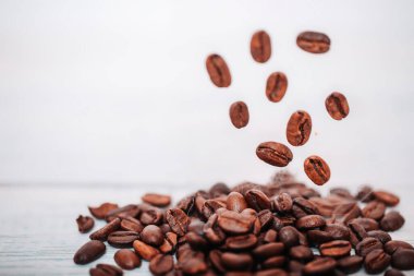 Kahverengi kahve çekirdekleri beyaz arka planda düşüp uçuyor. Bir kahve çekirdeğine odaklanmış kahve çekirdeği..