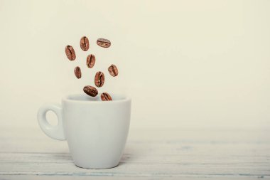 Kavrulmuş kahve çekirdekleri kahve fincanına dökülüyor. Beyaz arka plan, taze ve parlak duvar kağıdı konsepti. Kahve çekirdekleri beyaz fincana düşüyor. Yüksek hız görüntüsü.