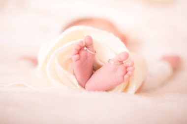 Yeni doğmuş bir bebeğin ayakları ve ailesinin alyansları. Yeni doğmuş bir bebeğin bacakları ve annesinin alyansı beyaz yün bir halıda. Mutlu Aile kavramı. Anneliğin güzel kavramsal görüntüsü. Resmi kapat.
