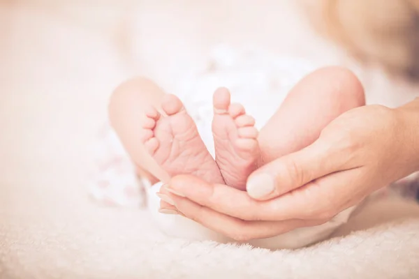 Newborn feet. Sweet baby in a gentle morning light on the bed. Bare feet of a cute newborn baby in warm white blanket. Childhood. Small bare feet of a little baby girl or boy. Sleeping newborn child.