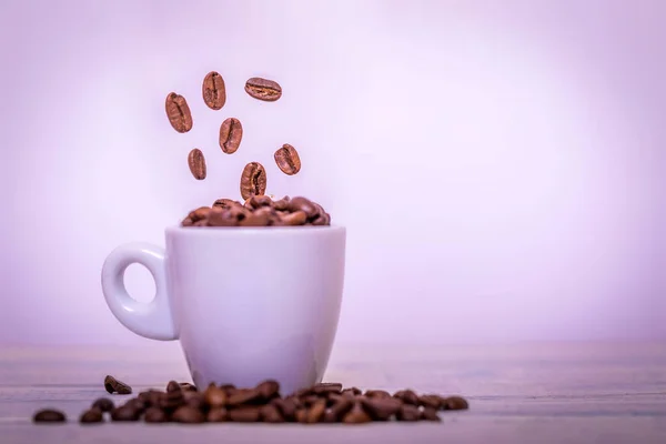 Coffee beans falling in white cup. Highspeed shot. Roasted coffee beans falling into coffee cup on saucer with white background, fresh energy wallpaper concept. Close up image.