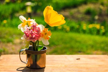 Tahta bir masada, çiçekli kırsal bardak, yaz bahçesi, rahatlama konsepti. Yaz bahçesinde kupada bahar çiçekleri. Kırsal alan, güneş ışığı altında. Yaz mevsimi.