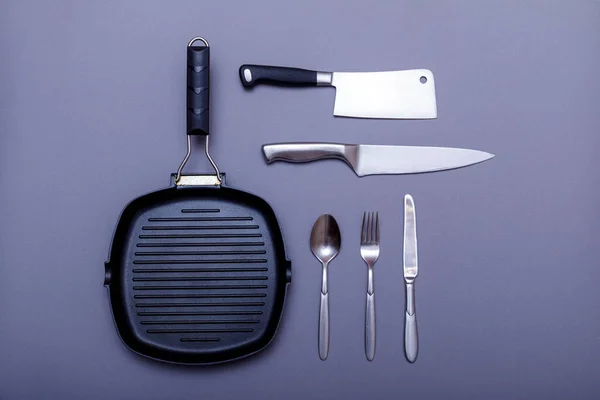 Metal knives with black on a grey table, grill pan, towel. Flat lay, layout with copy space. High resulotion image.