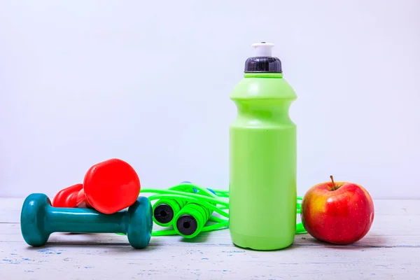 Green bottle of water, sports towel and exercise equipment isolated against a white background and wooden table. High resulotion image.