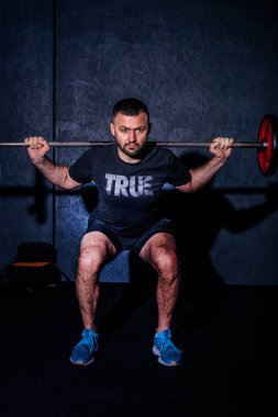 Spor salonunda halter kaldıran sakallı bir gencin ön görüntüsü. Güçlü ve sağlıklı yaşam tarzı konsepti. Yüksek resulotion resmi.