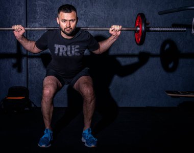 Spor salonunda halter kaldıran sakallı bir gencin ön görüntüsü. Güçlü ve sağlıklı yaşam tarzı konsepti. Yüksek resulotion resmi.