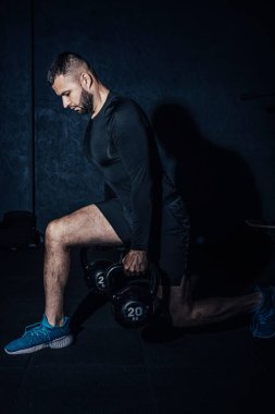 Atletik beyaz adam, çan kaldırırken çömeliyor. Genç kaslı adam spor salonunda kettlebell ile egzersiz yapıyor. Ağırlık kaldırma egzersizi. Spor, spor konsepti. Yüksek resulotion resmi.