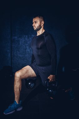 Atletik beyaz adam, çan kaldırırken çömeliyor. Genç kaslı adam spor salonunda kettlebell ile egzersiz yapıyor. Ağırlık kaldırma egzersizi. Spor, spor konsepti. Yüksek resulotion resmi.