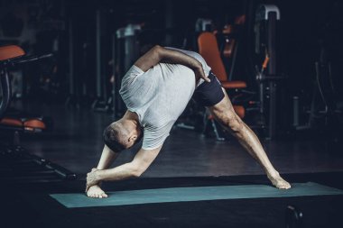 Sportif genç adam yoga yapıyor, esneme egzersizleri yapıyor, üçgen pozlar veriyor esnek omurga için utthita trikonasana asana ve spor salonundaki stresi azaltıyor. Yüksek resulotion resmi.