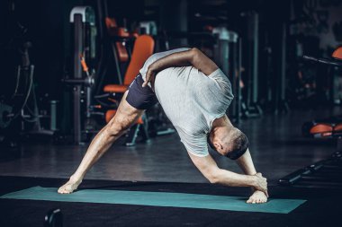 Sportif sakallı genç adam yoga yapıyor, esneme egzersizleri yapıyor, üçgen pozlar veriyor esnek omurga için utthita trikonasana asana ve spor salonundaki stresi azaltıyor. Yüksek resulotion resmi.