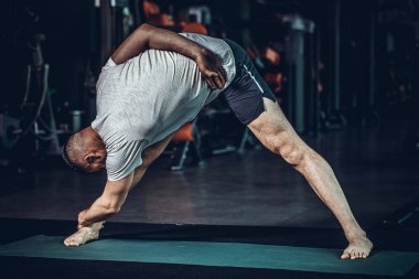 Sportif sakallı genç adam yoga yapıyor, esneme egzersizleri yapıyor, üçgen pozlar veriyor esnek omurga için utthita trikonasana asana ve spor salonundaki stresi azaltıyor. Yüksek resulotion resmi.