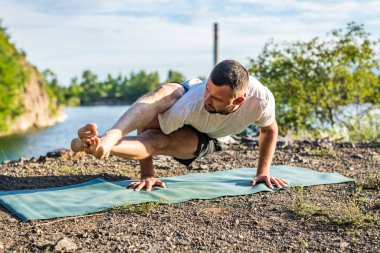 Sabah ve akşam yakışıklı genç bir adam yazın açık havada taş ocağı gölünün kıyısında yoga egzersizi yapıyor. Sağlıklı aktif yaşam tarzı kavramı.