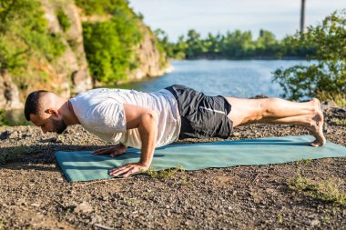 Sabah ve akşam yakışıklı genç bir adam yazın açık havada taş ocağı gölünün kıyısında yoga egzersizi yapıyor. Sağlıklı aktif yaşam tarzı kavramı.