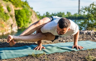 Sabah ve akşam yakışıklı genç bir adam yazın açık havada taş ocağı gölünün kıyısında yoga egzersizi yapıyor. Sağlıklı aktif yaşam tarzı kavramı.