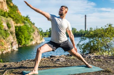 Elleri ve bacakları eşe uzatan bir adam. Sakallı adam taş ocağında ve dağlarda yoga yapıyor..