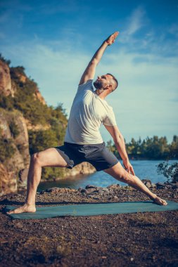 Elleri ve bacakları eşe uzatan bir adam. Sakallı adam taş ocağında ve dağlarda yoga yapıyor..