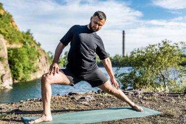 Elleri ve bacakları eşe uzatan bir adam. Sakallı adam taş ocağında ve dağlarda yoga yapıyor..