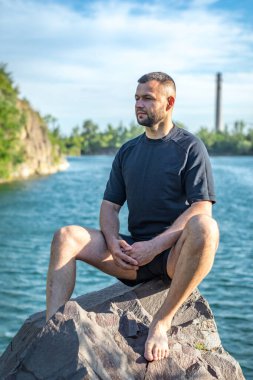 Taş ocağının arka planında kayaların üzerinde oturan sakallı genç adam. Yakışıklı portre..