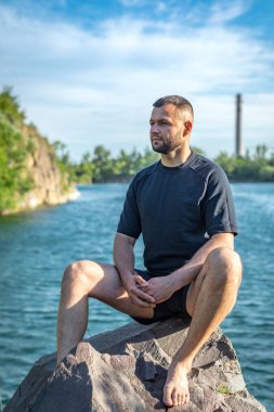Taş ocağının arka planında kayaların üzerinde oturan sakallı genç adam. Yakışıklı portre..
