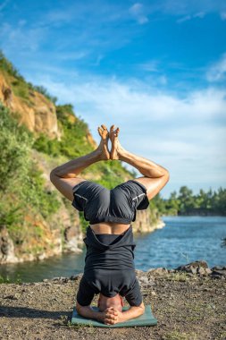 Sakallı, yakışıklı, siyah saçlı, yoga yapan bir adam. Kafasının üstünde duran genç adam Sirshasana 'nın taş ocağı gölünde durduğu pozda..