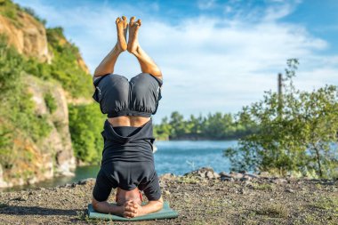 Sakallı, yakışıklı, siyah saçlı, yoga yapan bir adam. Kafasının üstünde duran genç adam Sirshasana 'nın taş ocağı gölünde durduğu pozda..