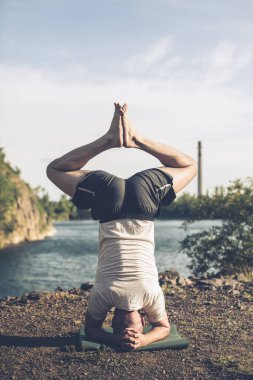 Güçlü sağlıklı atletik adam sabah antrenmanı yapıyor taş ocağı gölünde yoga yapıyor, baş aşağı duruyor. Rahatlama ve meditasyon, sağlıklı yaşam tarzı konsepti. Uluslararası Yoga Günü.