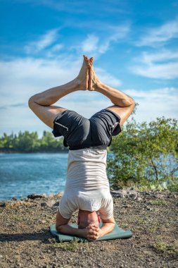 Güçlü sağlıklı atletik adam sabah antrenmanı yapıyor taş ocağı gölünde yoga yapıyor, baş aşağı duruyor. Rahatlama ve meditasyon, sağlıklı yaşam tarzı konsepti. Uluslararası Yoga Günü.
