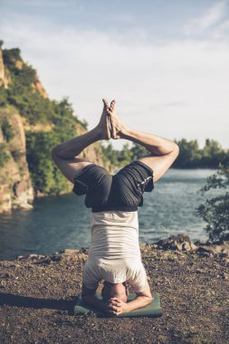 Güçlü sağlıklı atletik adam sabah antrenmanı yapıyor taş ocağı gölünde yoga yapıyor, baş aşağı duruyor. Rahatlama ve meditasyon, sağlıklı yaşam tarzı konsepti. Uluslararası Yoga Günü.