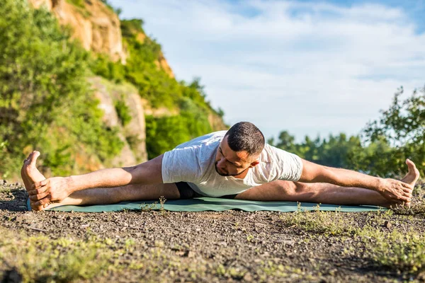 Young fitness man doing yoga exercise outdoors at the quarry lake. Handsome young man with a beard doing yoga exercise.