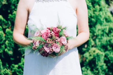 Gelin elinde güllerden bir buket tutuyor, düğün çiçekleri. Güzel bohem düğün çiçeği buketi. Bir buket gülü elbisesi olan kız..